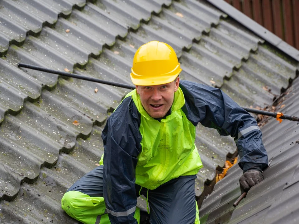 Roof professional examining a roof while wearing a helmet and fall-protection equipment