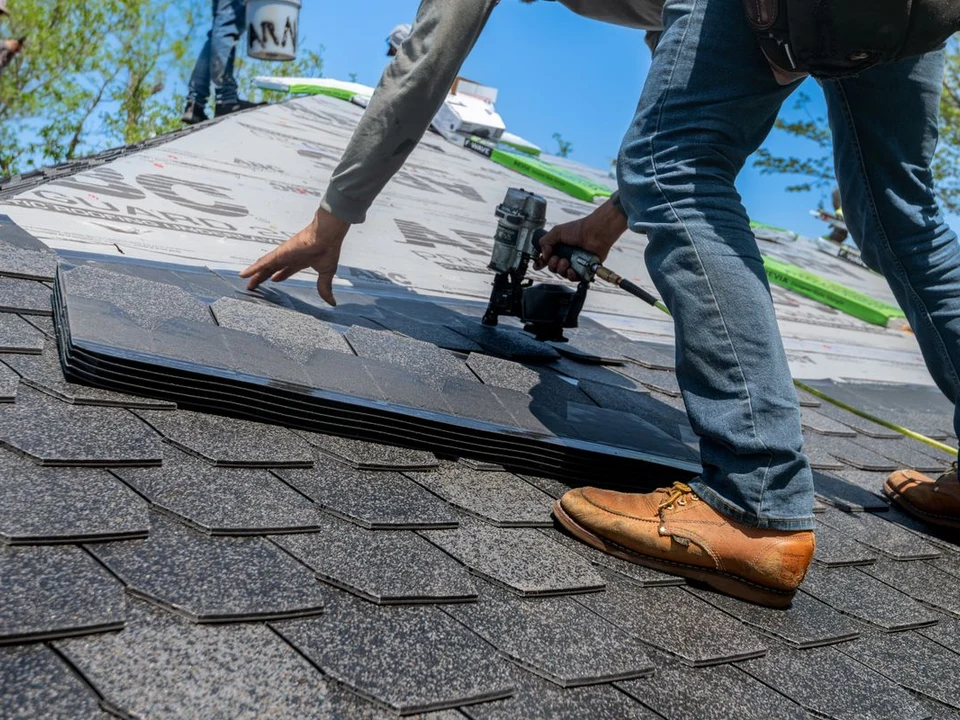 Close-up of a professional roofer fastening replacement architectural shingles